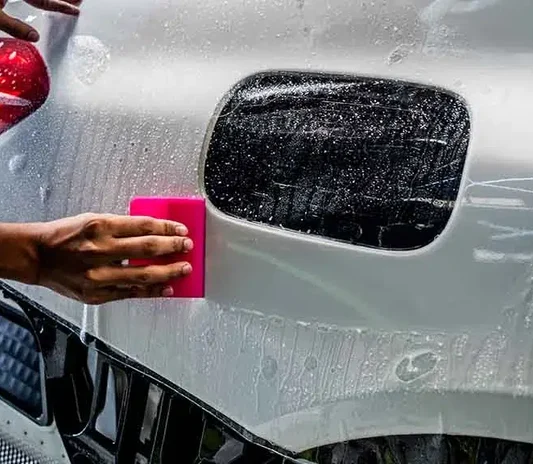 Paint protection film being squeegeed onto a fender near the fuel cap on a white car in Dubai